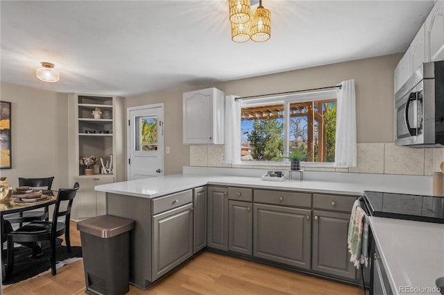 kitchen featuring range with electric stovetop, light wood-type flooring, a peninsula, stainless steel microwave, and gray cabinets