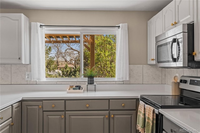 kitchen featuring appliances with stainless steel finishes, gray cabinetry, backsplash, and a healthy amount of sunlight