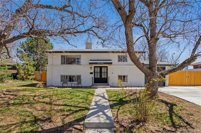 view of front of home featuring a chimney, a front yard, fence, brick siding, and french doors