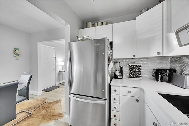 kitchen with sink, stainless steel fridge, white cabinetry, decorative backsplash, and light hardwood / wood-style flooring