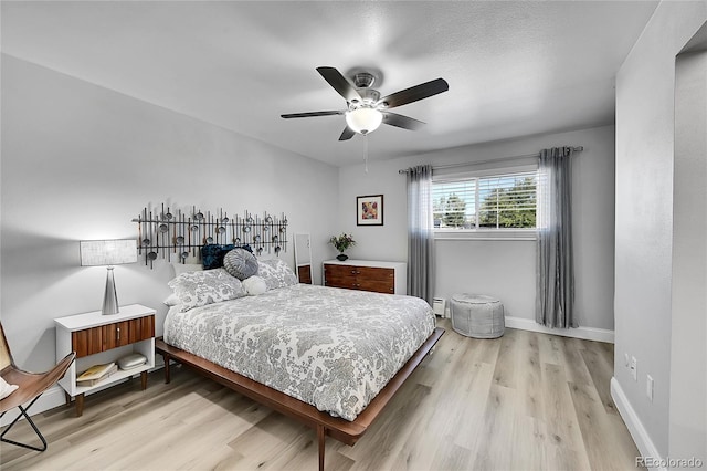 bedroom with light hardwood / wood-style flooring, a baseboard heating unit, and ceiling fan