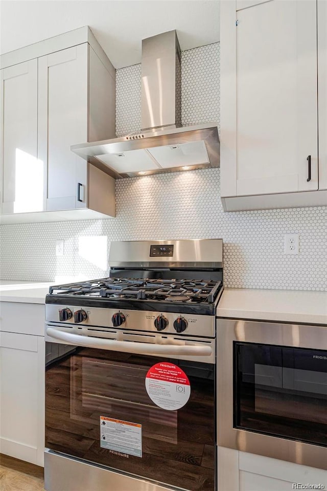 kitchen with wall chimney exhaust hood, white cabinetry, backsplash, and appliances with stainless steel finishes