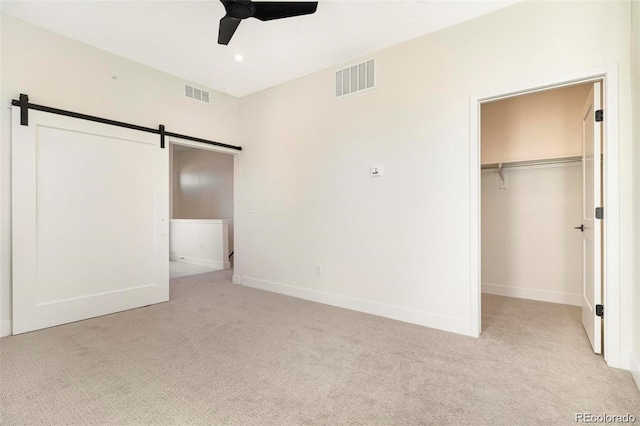 unfurnished bedroom featuring light carpet, a walk in closet, ceiling fan, a barn door, and a closet