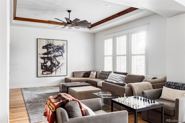 living room featuring hardwood / wood-style flooring, ceiling fan, ornamental molding, and a tray ceiling