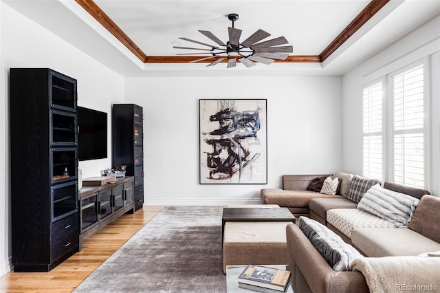 living room with ceiling fan, ornamental molding, light wood-type flooring, and a tray ceiling