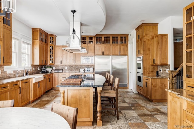 kitchen featuring decorative backsplash, stainless steel appliances, hanging light fixtures, and an island with sink