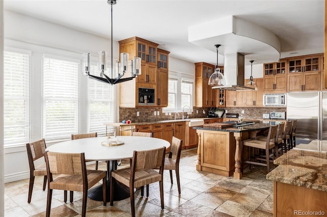 kitchen with built in appliances, tasteful backsplash, island range hood, a center island, and pendant lighting