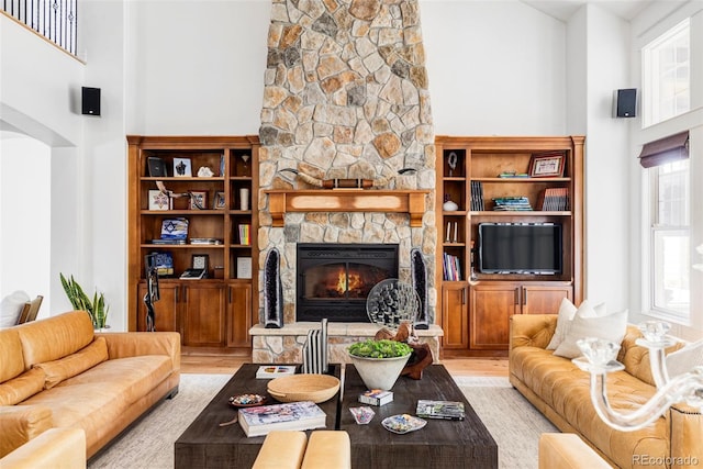 living room featuring a towering ceiling, a fireplace, a wealth of natural light, and light hardwood / wood-style flooring