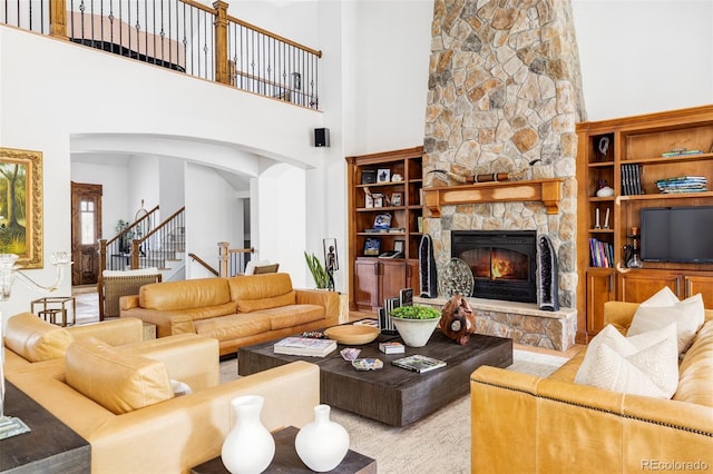 living room with a high ceiling, a stone fireplace, and built in shelves