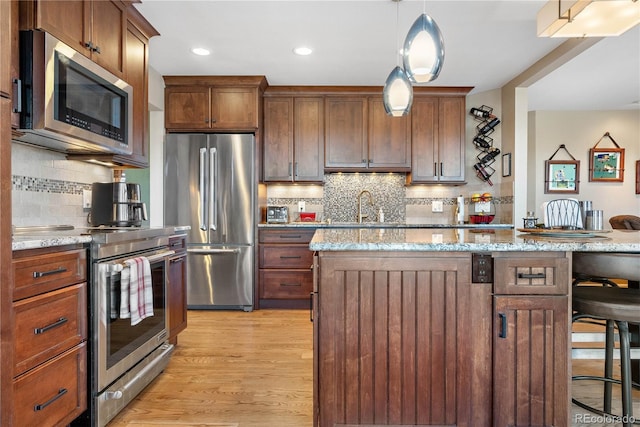 kitchen with appliances with stainless steel finishes, light wood-style floors, a breakfast bar area, and light stone countertops