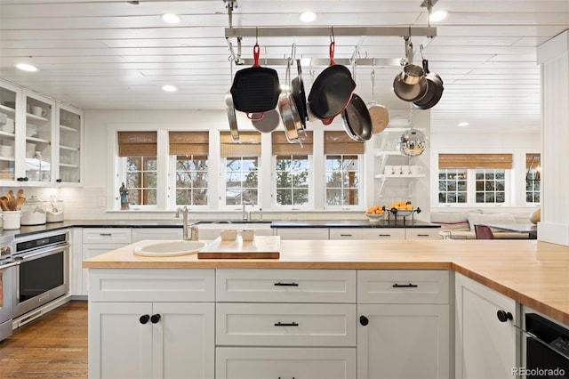 kitchen with sink, white cabinets, oven, and butcher block countertops