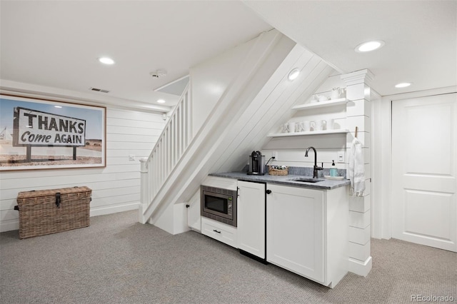 bar featuring sink, white cabinets, stainless steel microwave, and light carpet