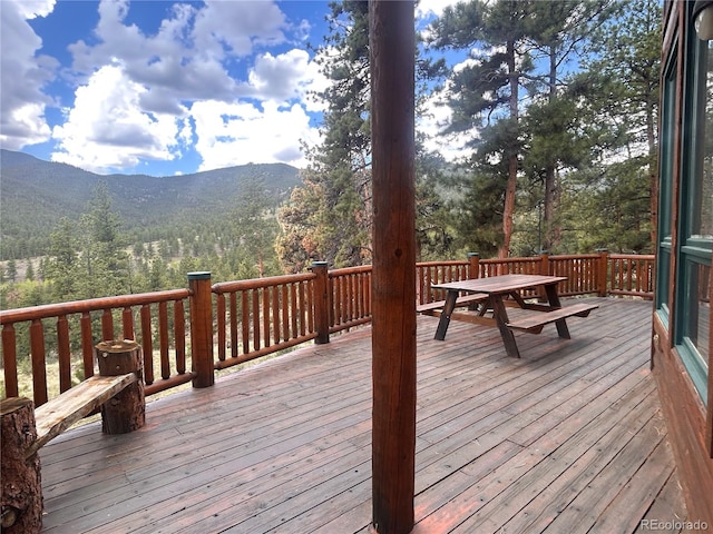 wooden terrace with a mountain view, outdoor dining area, and a view of trees