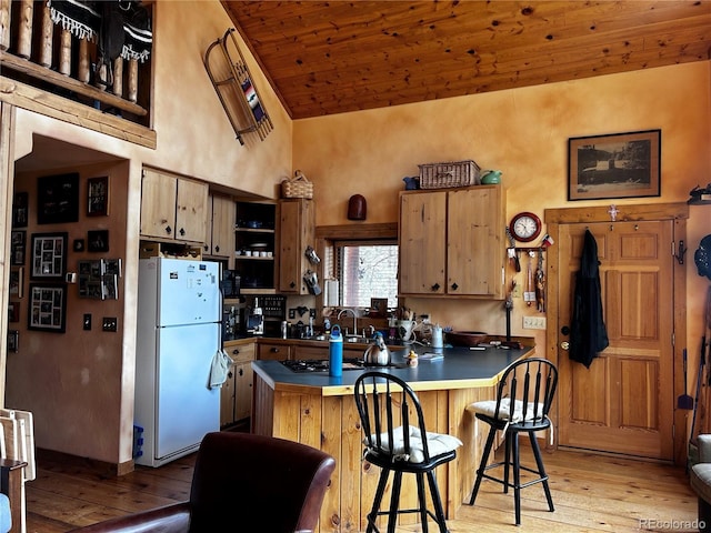 kitchen featuring freestanding refrigerator, wood ceiling, high vaulted ceiling, light wood-style flooring, and a kitchen breakfast bar