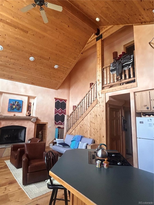 living area featuring a wood ceiling with exposed beams, wood-type flooring, a fireplace, a ceiling fan, and stairway