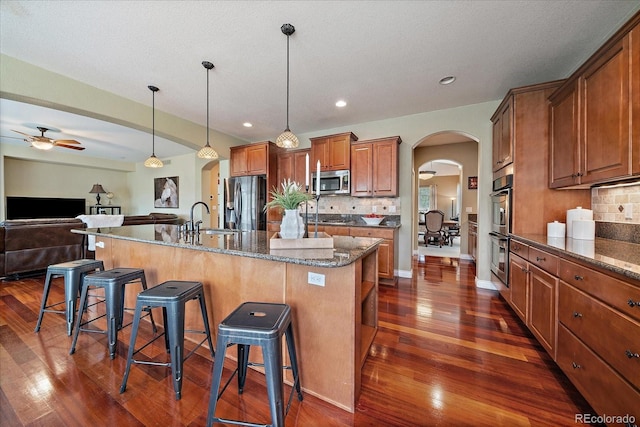15258 W 75th Pl, Arvada, CO 80007 - kitchen with stainless steel appliances, arched walkways, a kitchen bar, open floor plan, and brown cabinets