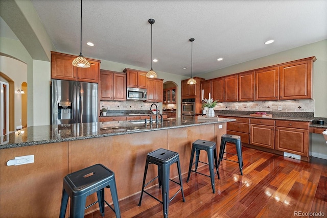 15258 W 75th Pl, Arvada, CO 80007 - kitchen with stainless steel appliances, arched walkways, a sink, brown cabinets, and dark wood finished floors