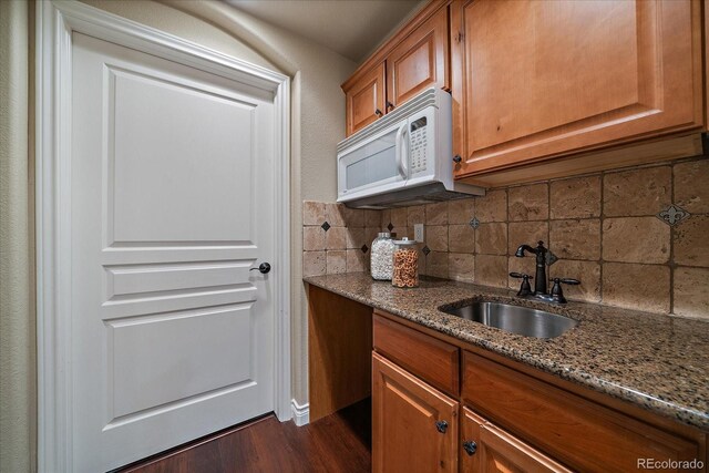 15258 W 75th Pl, Arvada, CO 80007 - kitchen with white microwave, a sink, dark stone counters, brown cabinetry, and decorative backsplash