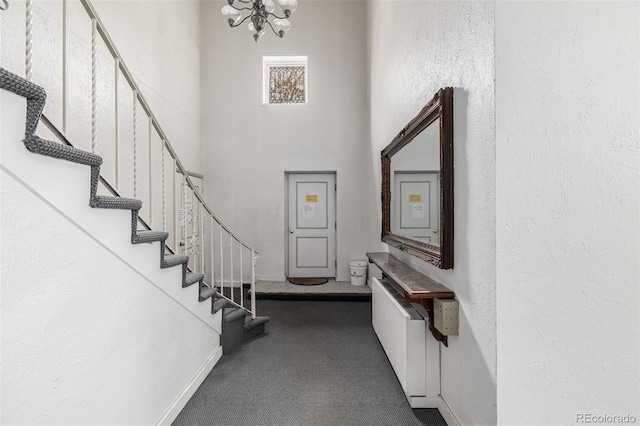 carpeted entrance foyer featuring a textured wall, stairway, a high ceiling, and an inviting chandelier