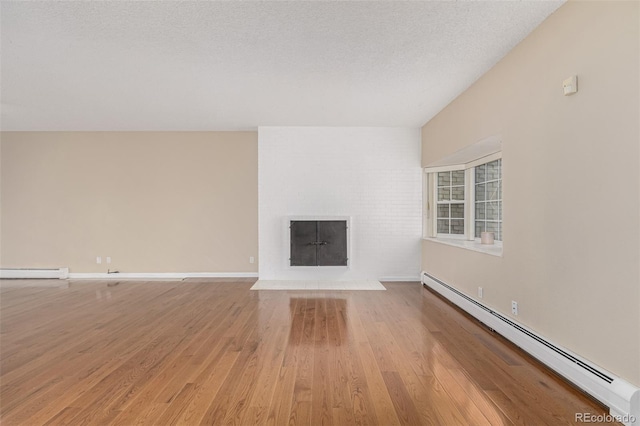 unfurnished living room featuring a textured ceiling, a fireplace, a baseboard radiator, and wood finished floors