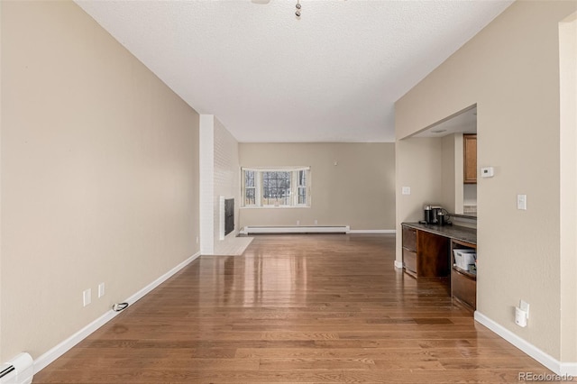 unfurnished living room with a baseboard heating unit, a fireplace, wood finished floors, and baseboards