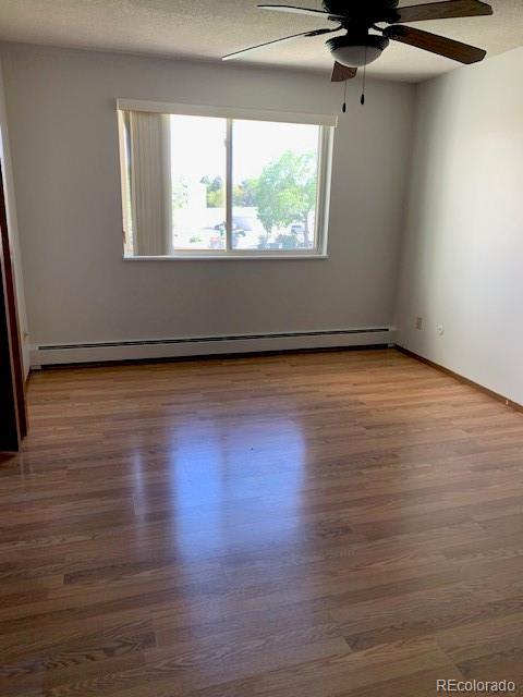 empty room with baseboard heating, a ceiling fan, wood finished floors, and baseboards