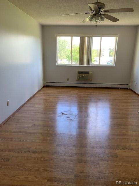 spare room with wood finished floors, a wall unit AC, a ceiling fan, and baseboards