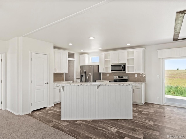 kitchen featuring white cabinets, a center island with sink, appliances with stainless steel finishes, and dark hardwood / wood-style flooring