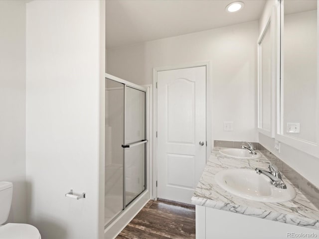 bathroom featuring a shower with shower door, double vanity, toilet, and wood-type flooring