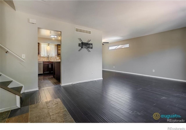 unfurnished living room featuring visible vents, a sink, stairs, baseboards, and dark wood-style floors