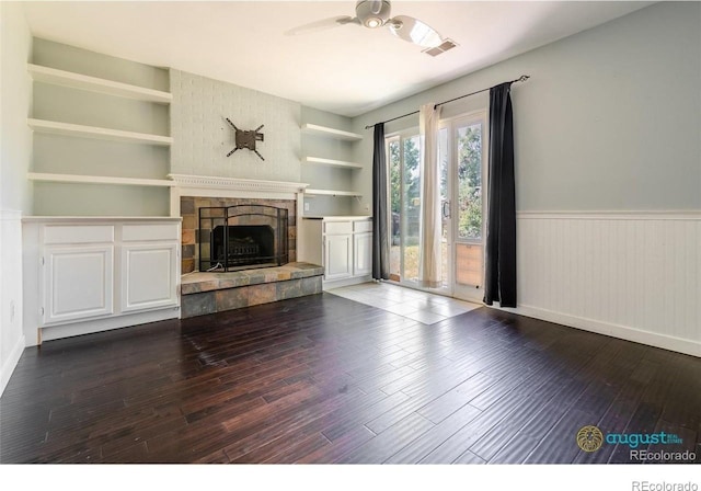 unfurnished living room featuring a stone fireplace, wainscoting, visible vents, hardwood / wood-style floors, and ceiling fan