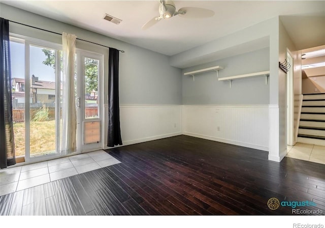 spare room with visible vents, ceiling fan, hardwood / wood-style flooring, stairway, and wainscoting