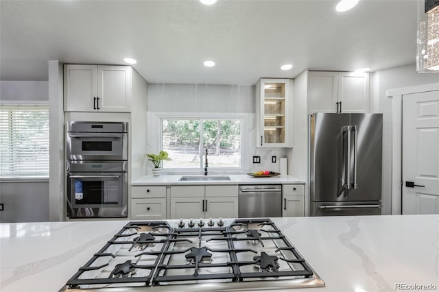 kitchen featuring appliances with stainless steel finishes, light stone counters, white cabinetry, and sink