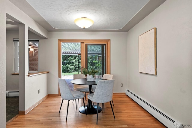 dining area with light wood-type flooring, a textured ceiling, and baseboard heating