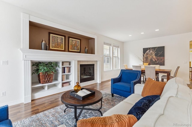 living room with built in shelves, wood-type flooring, and a tile fireplace