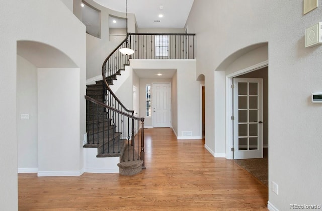 entrance foyer featuring baseboards, arched walkways, a towering ceiling, wood finished floors, and stairs