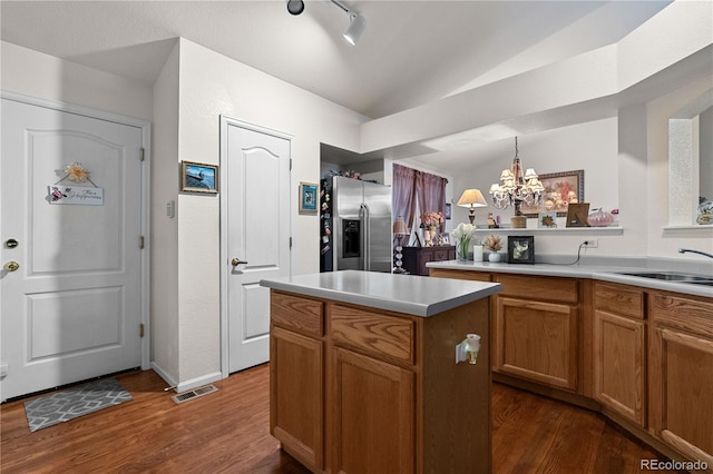 kitchen featuring stainless steel fridge with ice dispenser, a center island, hanging light fixtures, light countertops, and a sink