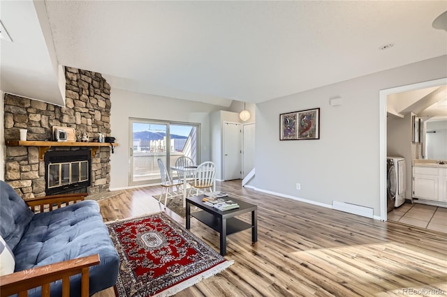 living room featuring sink, baseboard heating, washer / clothes dryer, a fireplace, and light wood-type flooring