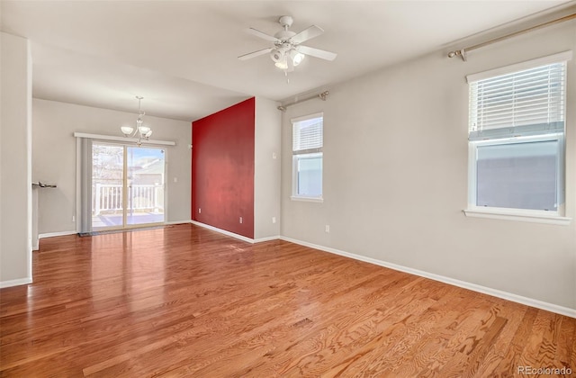 empty room with hardwood / wood-style flooring, ceiling fan with notable chandelier, and a wealth of natural light