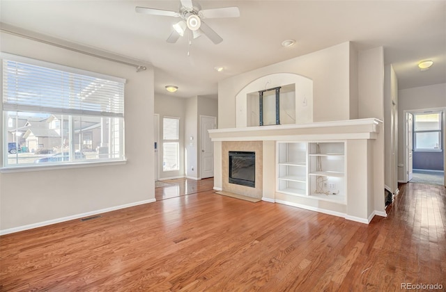 unfurnished living room featuring hardwood / wood-style floors, ceiling fan, and a tiled fireplace