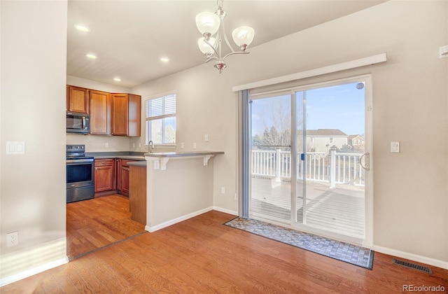 kitchen featuring stainless steel range with electric cooktop, an inviting chandelier, hanging light fixtures, a kitchen bar, and kitchen peninsula