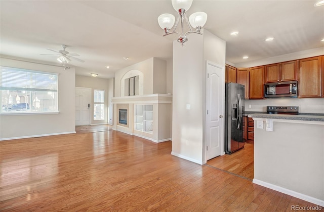 kitchen featuring pendant lighting, ceiling fan with notable chandelier, a fireplace, appliances with stainless steel finishes, and light hardwood / wood-style floors