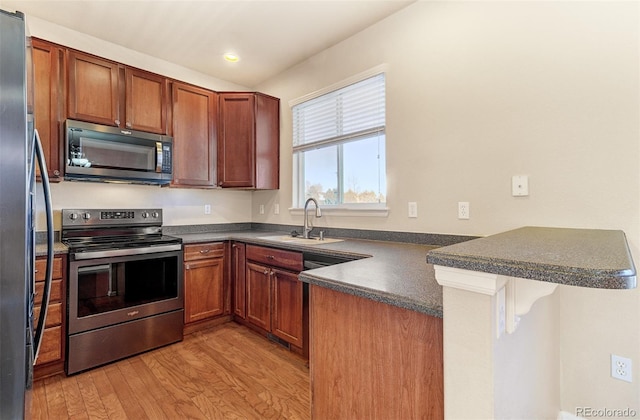 kitchen with sink, stainless steel appliances, kitchen peninsula, a breakfast bar, and light wood-type flooring