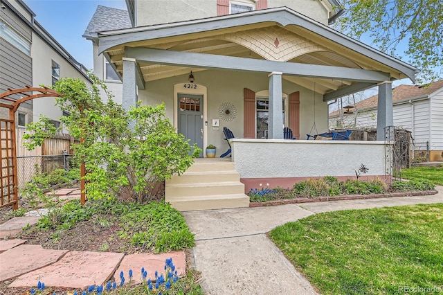 view of front of home with stucco siding, covered porch, and fence