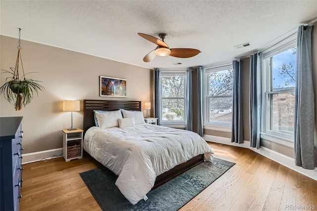bedroom featuring visible vents, a ceiling fan, light wood-style floors, baseboards, and a textured ceiling