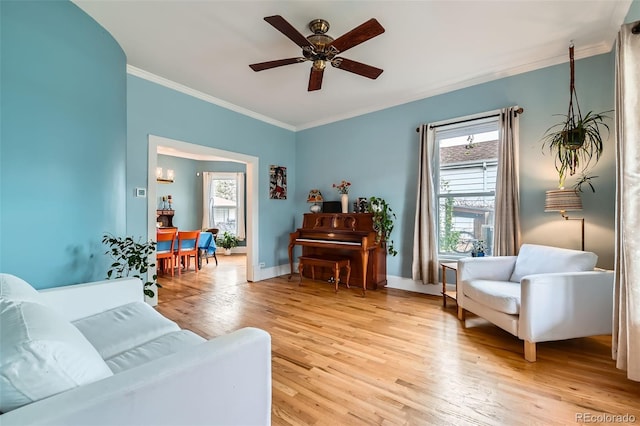 living room featuring ceiling fan, baseboards, crown molding, and light wood-style floors