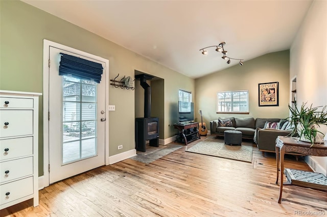 living room with vaulted ceiling, track lighting, a wood stove, light wood finished floors, and baseboards