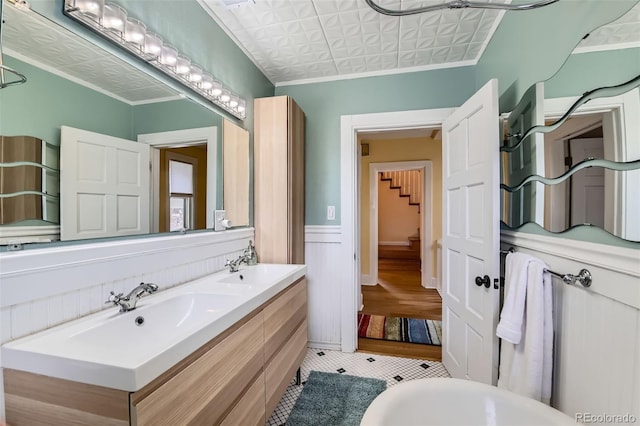 full bathroom featuring double vanity, a wainscoted wall, ornamental molding, and a sink