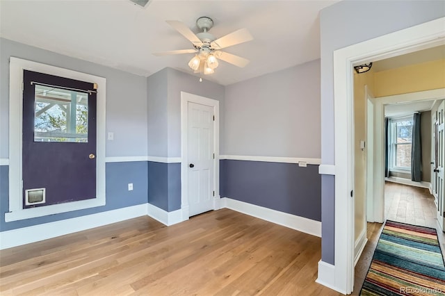 spare room featuring light wood finished floors, a ceiling fan, baseboards, and a wealth of natural light