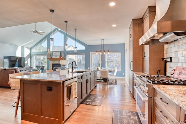 kitchen featuring light wood-type flooring, sink, wall chimney range hood, stainless steel stove, and hanging light fixtures